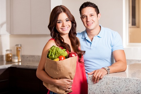 Beautiful young woman and her partner carrying a bag of groceries in the kitchenの写真素材
