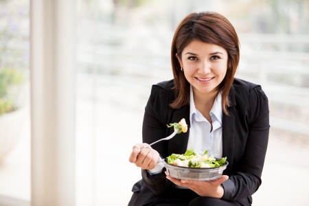 Happy young business woman enjoying a healthy salad at workの写真素材