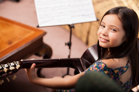 Beautiful little Hispanic girl playing the guitar at homeの写真素材