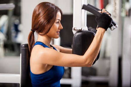 Cute young woman wearing a sporty outfit and gloves working out in a simulator at the gymの写真素材