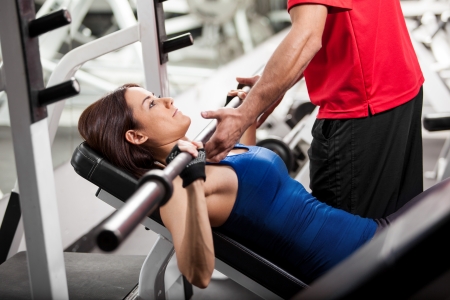 Personal trainer helping a young woman lift a barbell while working out in a gymの写真素材
