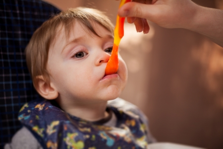 Adorable blonde baby boy in a bib being fed by his momの写真素材
