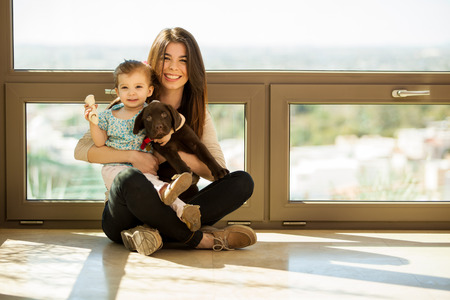 Beautiful young mother sitting at home with her daughter and their cute Labrador puppy
