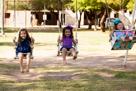 Happy little Latin girls having fun in a swing outdoors in summerの写真素材