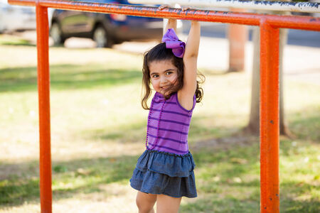Pretty little girl climbing and hanging from some handlebars at a park