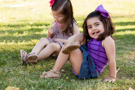Funny little girl relaxing and eating a lollipop with a friend at a parkの写真素材