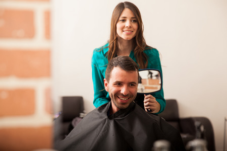 Happy customer looking at himself in a mirror after getting a haircut in a barber shopの写真素材
