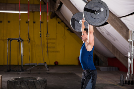 Profile view of a strong young man lifting some weights in a crossfit gymの写真素材