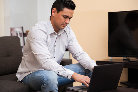 Young Latin man working from home using a laptop computer in the living roomの写真素材