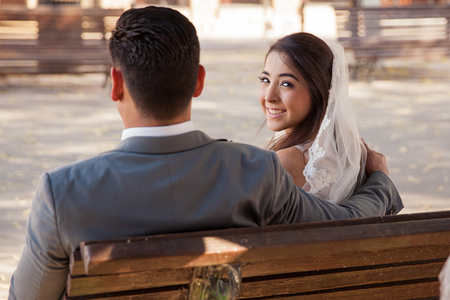 Portrait of a happy bride sitting on a bench with the groom and looking backの写真素材
