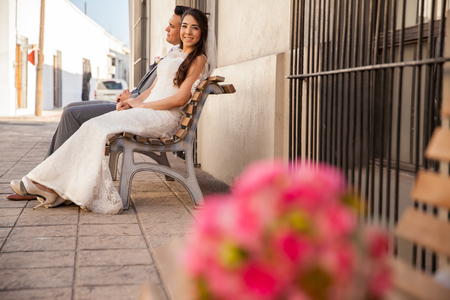 Happy bride and groom sitting on a bench outdoors with a flower bouquet on the foregroundの写真素材