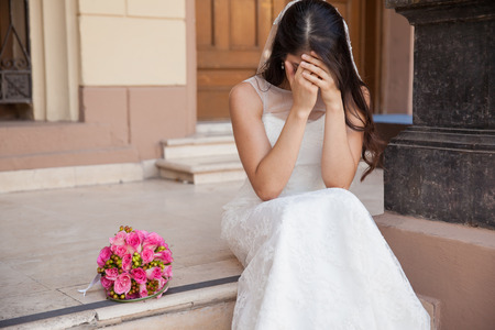 Hopeless bride crying outside a church after being stood up on her wedding dayの写真素材