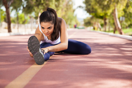 Hispanic young woman warming up and stretching at a running track outdoors