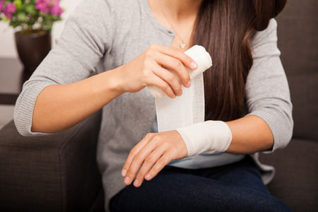Closeup of a young woman removing a bandage from her arm at homeの写真素材