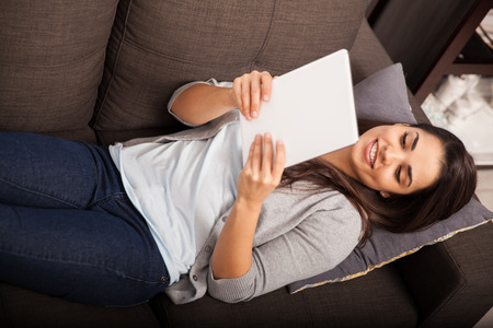 Top view of a cute young woman laying on a couch and reading on tablet computerの写真素材