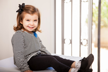 Portrait of a beautiful Hispanic little girl sitting on a table and waiting at the doctorの写真素材
