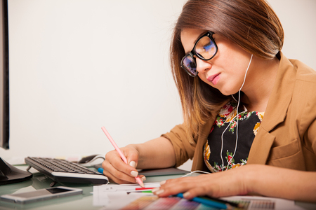 Pretty brunette doing some design work at an office while listening to musicの写真素材