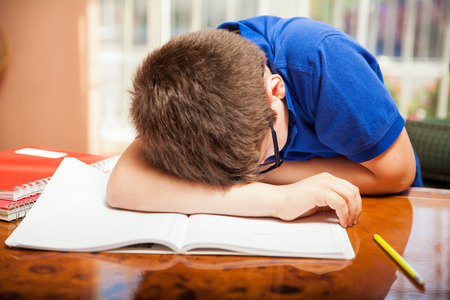 Little blond boy taking a nap in the middle of a difficult homeworkの写真素材