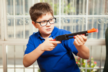 Funny little boy playing with a toy rifle and about to shoot a dartの写真素材