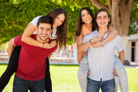 Group of college friends having fun. Men giving a piggyback ride to the girls at schoolの写真素材
