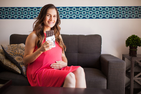 Cute young pregnant woman craving a bar of chocolate and smilingの写真素材
