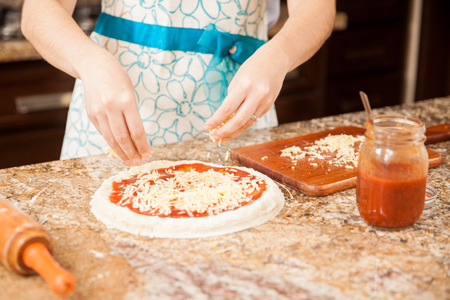 Closeup of the hands of a woman adding some cheese to her homemade pizzaの写真素材