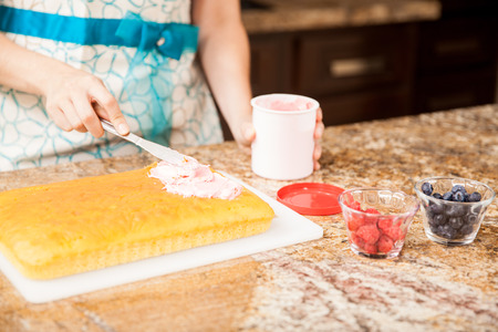Closeup of a young woman adding some pink frosting to a recently baked cake