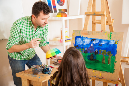 Handsome young art teacher talking about colors with a little girl during classの写真素材