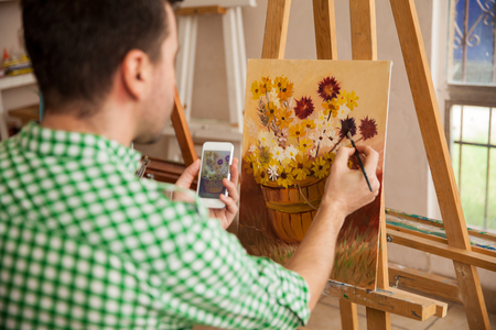 Point of view of a man copying an image from his smartphone into a painting of hir own for an art classの写真素材