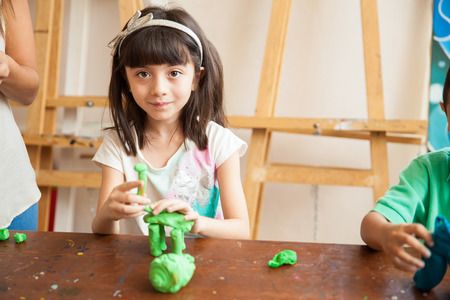 Portrait of a pretty little girl sculpting a house out of clay as part of her art classの写真素材