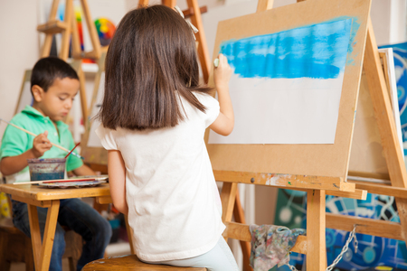 Rear view of a little girl painting the sky of a landscape for her art classの写真素材