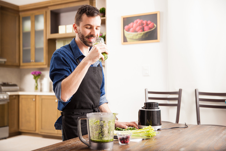 Happy guy in an apron drinking a healthy green smoothie at homeの写真素材
