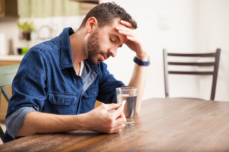 Good looking man with a beard feeling sick with indigestion and about to drink an effervescent tablet at home