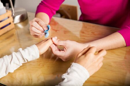 Closeup of the hands of a manicurist removing nail polish from the hands of a customer at a salon
