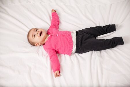 Portrait from above of a happy baby girl relaxing and spreading her arms and legs on a bed