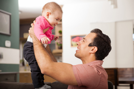 Profile view of a young father lifting her baby girl in the air and looking at herの写真素材