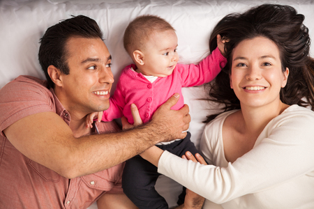 Beautiful young woman relaxing in a bed at home with her husband and her baby daughterの写真素材