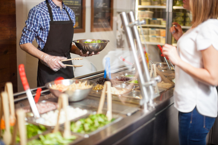 Closeup of a young man working at a restaurant and making a custom salad for a customerの写真素材