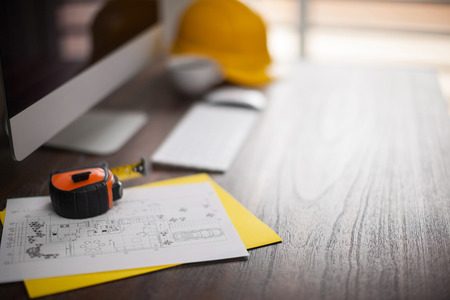 Computer, building plans, helment and tape measure in an architect's workspace with shallow depth of...