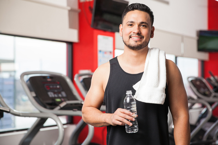 Portrait of a Hispanic young man taking a break and drinking some water after exercising in a gymの写真素材