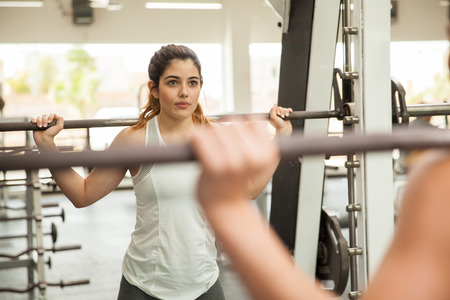 Portrait of a cute young woman working out on a squat machine at the gymの写真素材