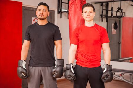 Portrait of two young Latin men wearing boxing gloves and about to fight each other at a gymの写真素材