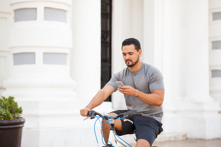 Young man getting distracted by his smartphone while riding his bicycle around the cityの写真素材