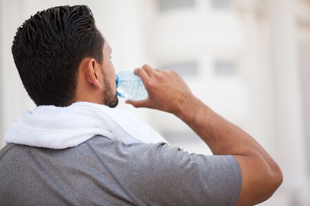 Rear view of a young man drinking water from a bottle after running and exercising outdoors