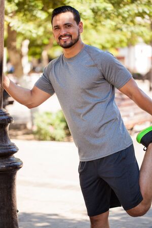 Attractive young Latin runner doing some stretching exercises and working out at a parkの写真素材