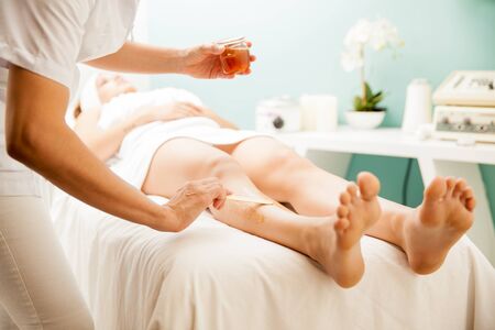 Closeup of a female therapist putting some honey on a woman's legs for removing her hair at a beauty...
