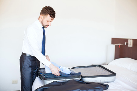 Good looking young businessman with a beard packing a suitcase and getting ready to leave the hotelの写真素材