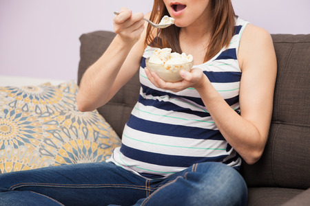 Closeup of a young pregnant woman eating a spoonful of ice cream while relaxing at homeの写真素材