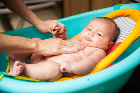 Closeup of the hands of a woman and mother giving a bath to her newborn baby in a bathtubの写真素材