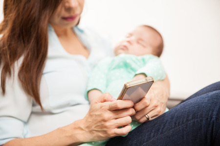 Closeup of a woman using her smartphone while her baby takes a nap. Focus on smartphone